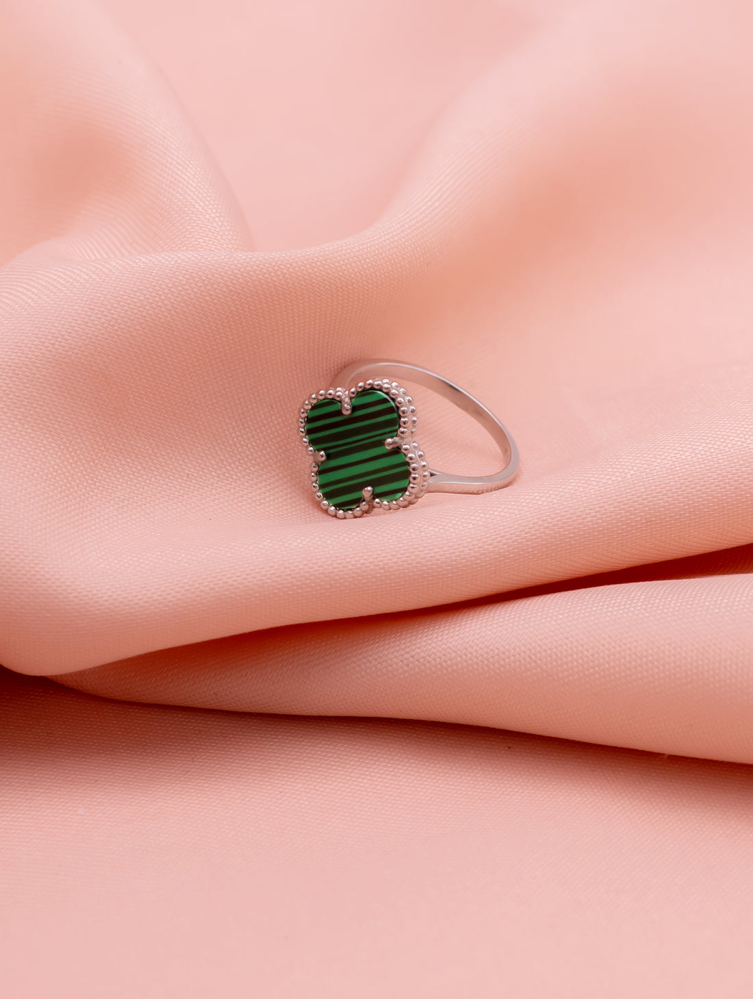 Ring with a green gemstone on a pink fabric background