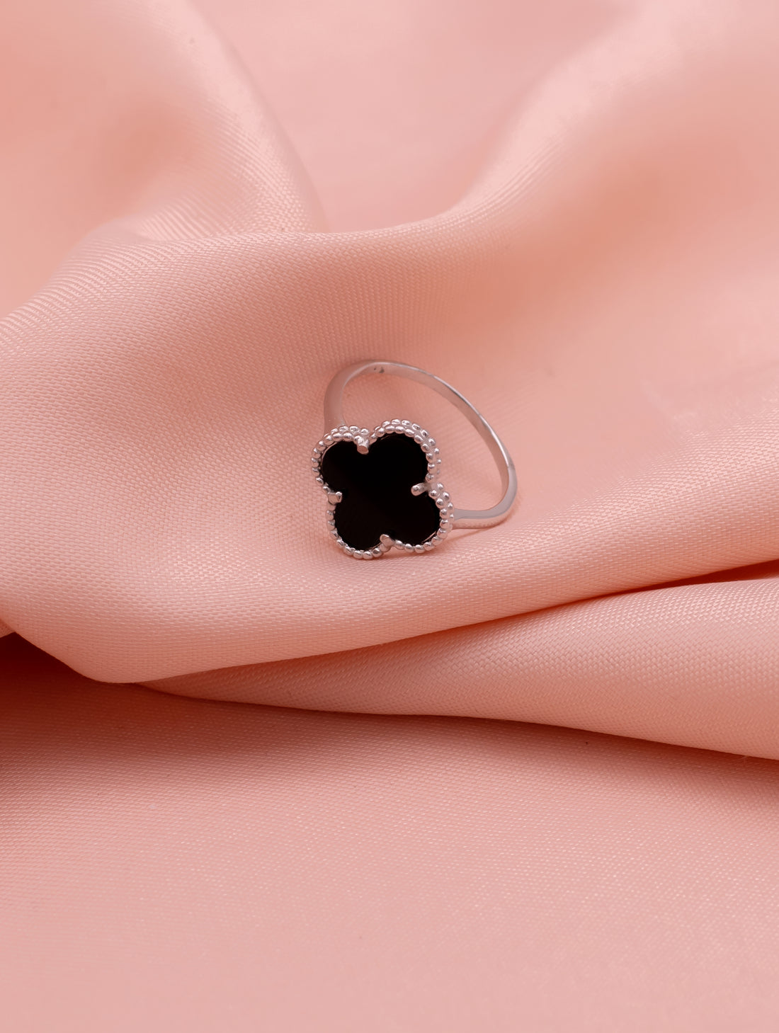 Silver ring with a black clover-shaped stone on a pink fabric background