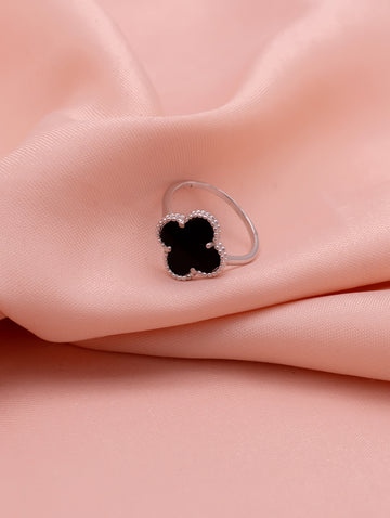 Silver ring with a black clover-shaped stone on a pink fabric background