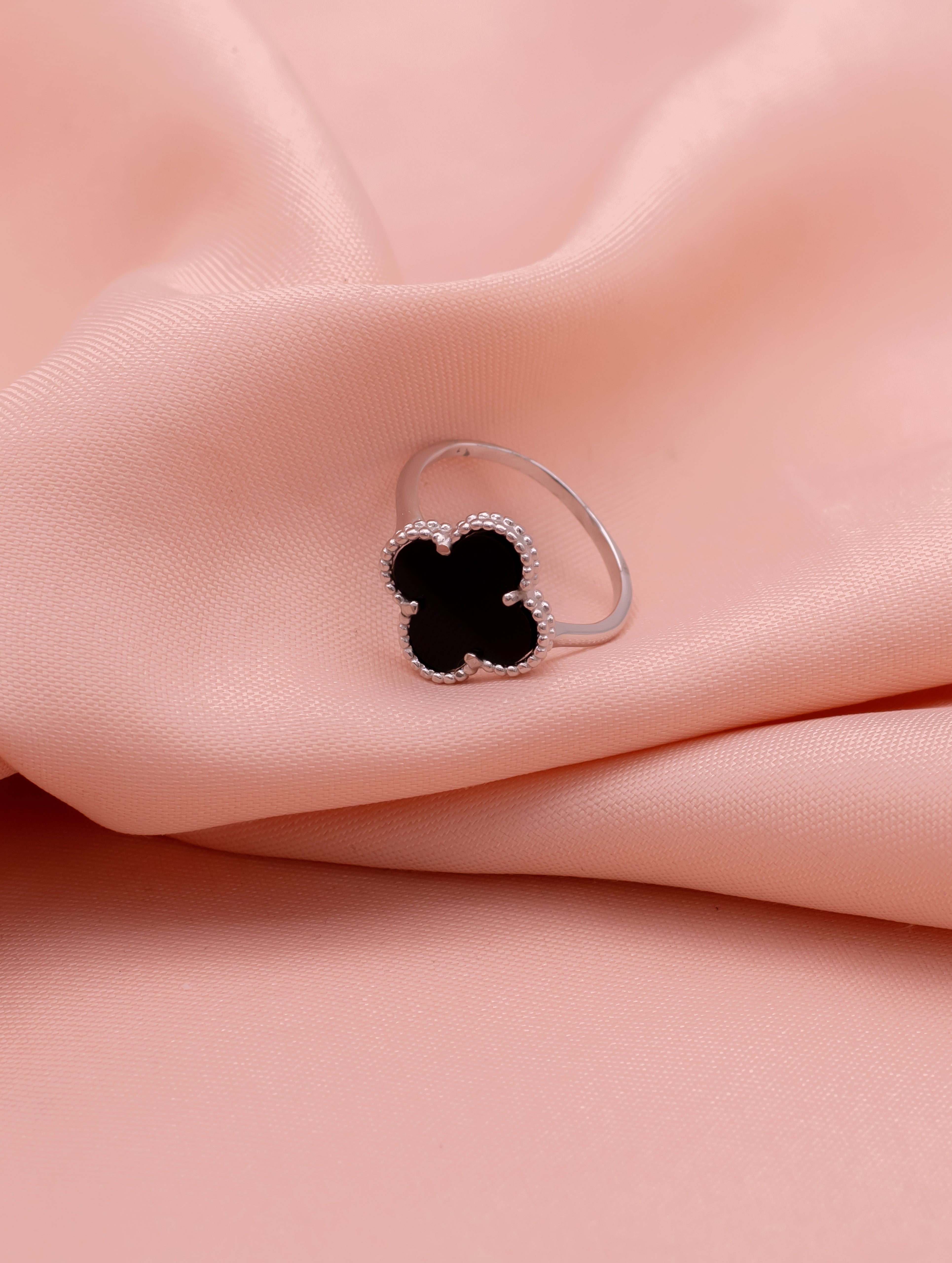 Silver ring with a black clover-shaped stone on a pink fabric background
