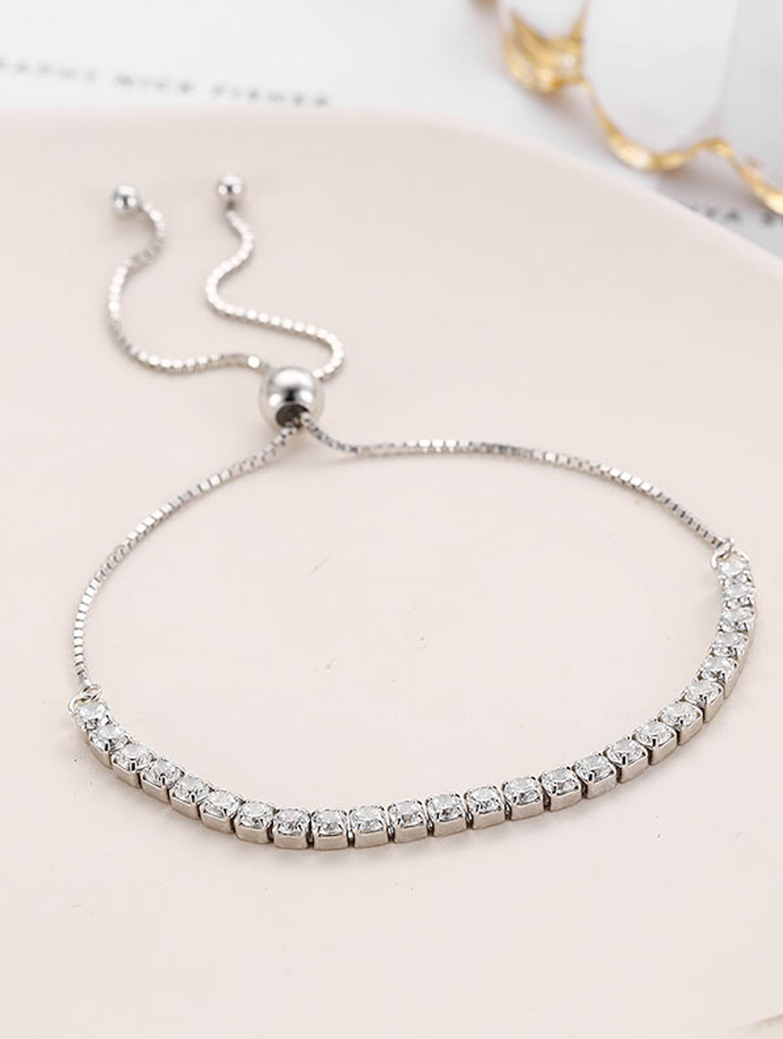 Silver bracelet with clear stones on a light pink surface