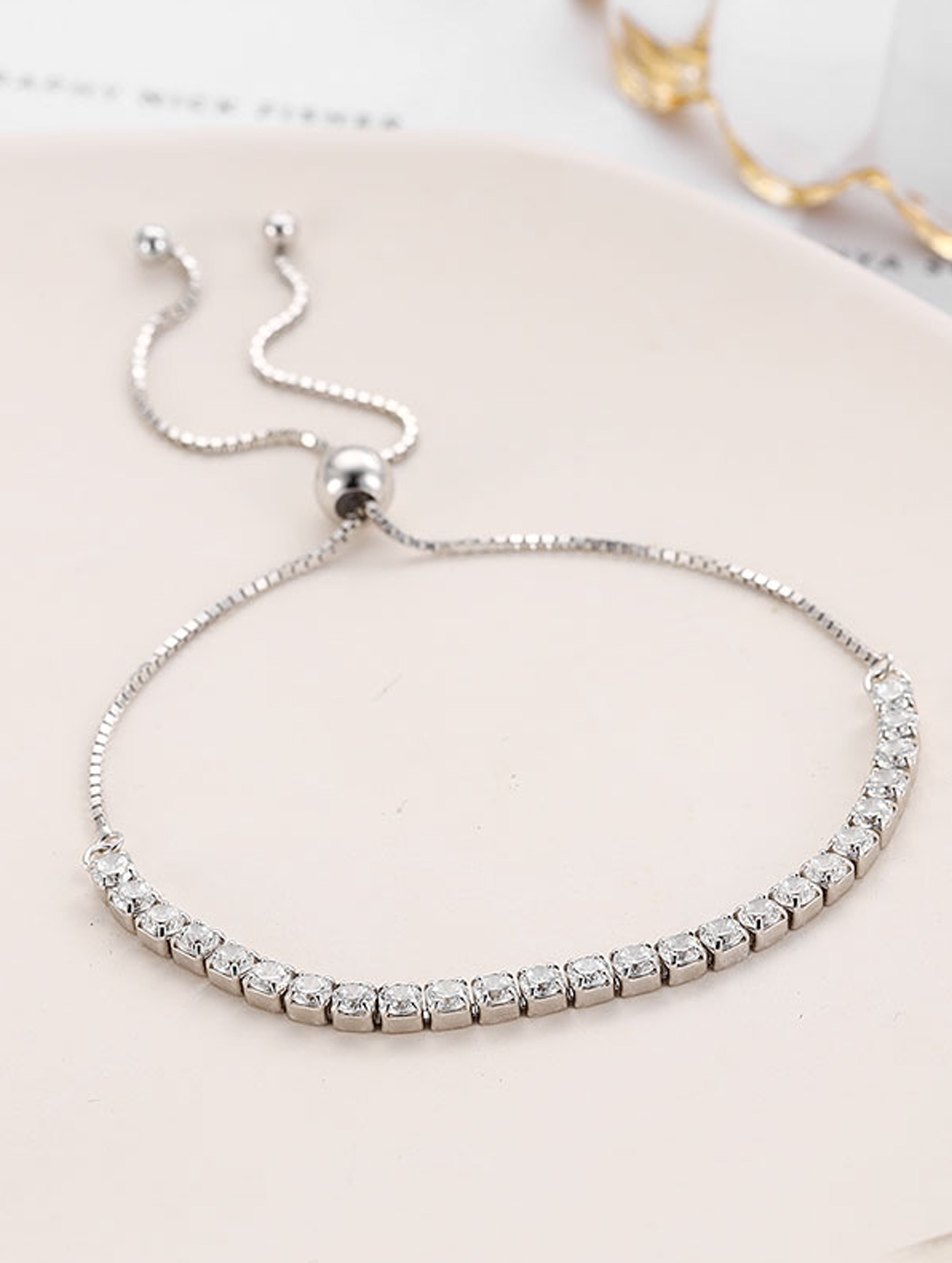 Silver bracelet with clear stones on a light pink surface