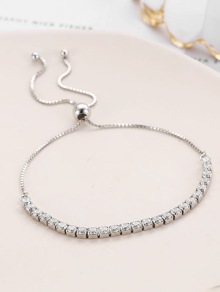 Silver bracelet with clear stones on a light pink surface