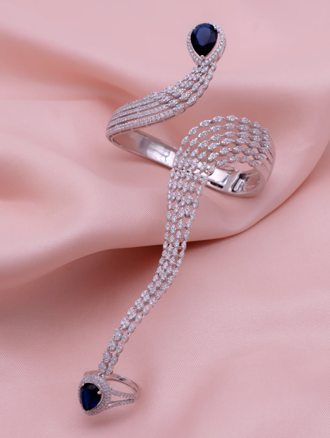 Silver snake-shaped ring with blue gemstones on a pink fabric background