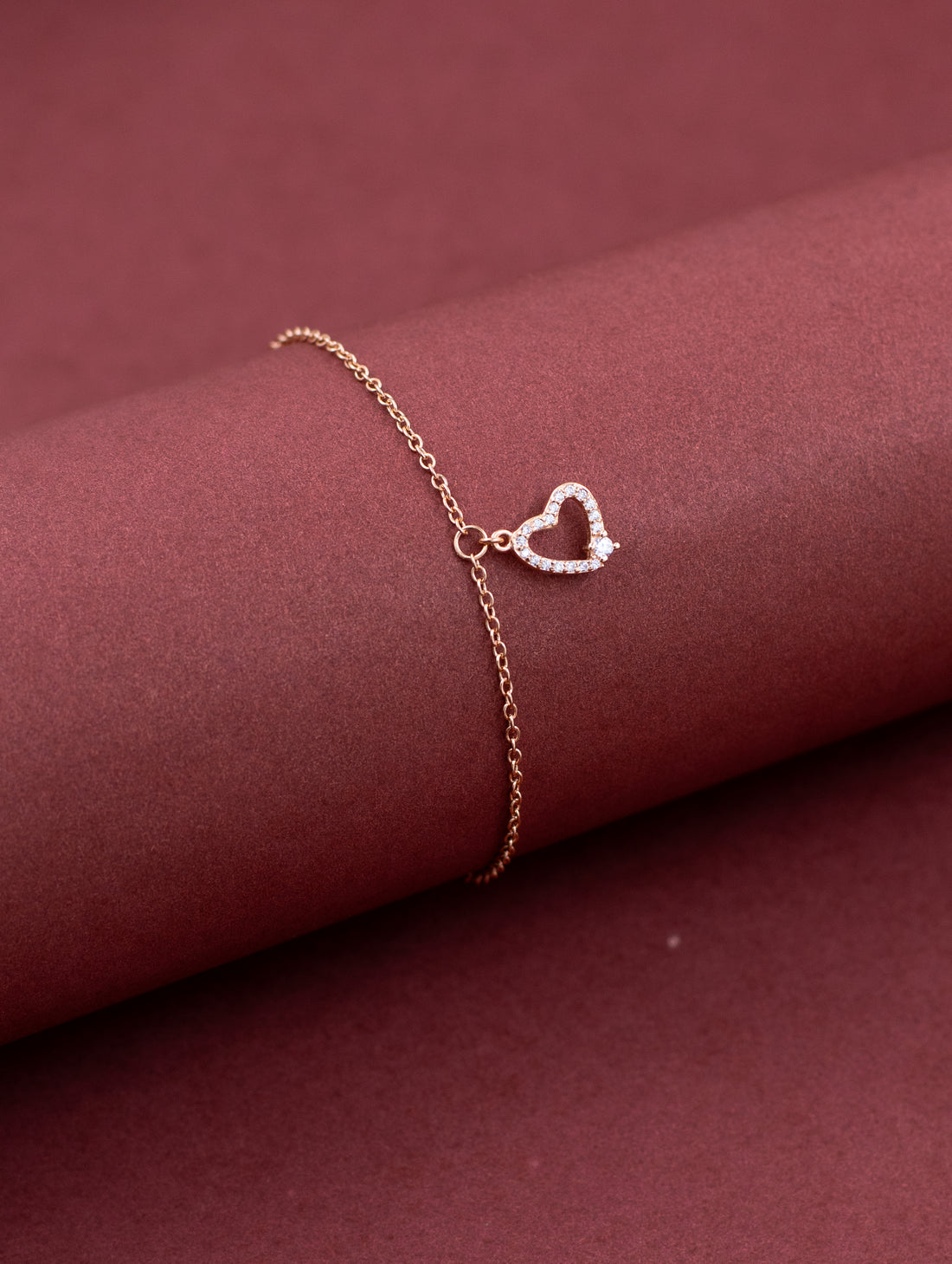 Rose gold bracelet with a heart-shaped clasp on a maroon fabric background