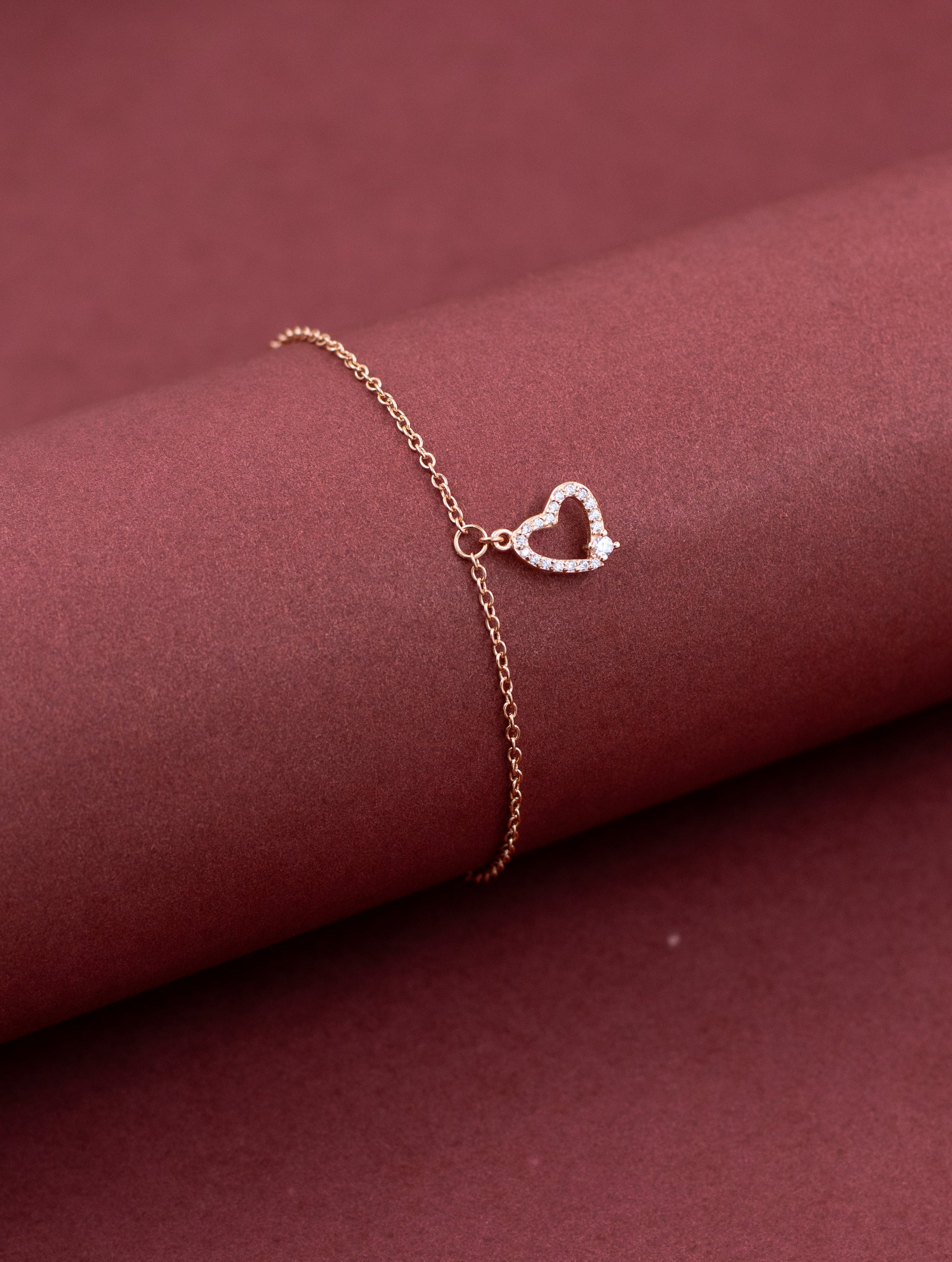 Rose gold bracelet with a heart-shaped clasp on a maroon fabric background