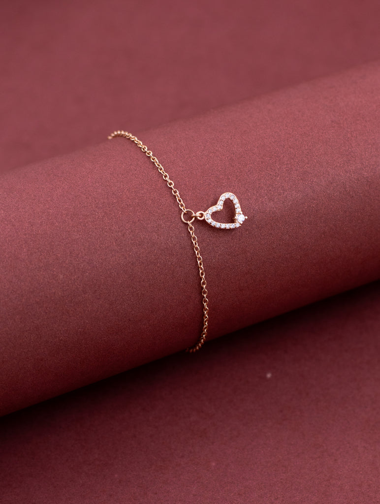 Rose gold bracelet with a heart-shaped clasp on a maroon fabric background